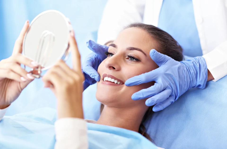A young woman with braces and long brown hair smiling while sitting in a dental chair