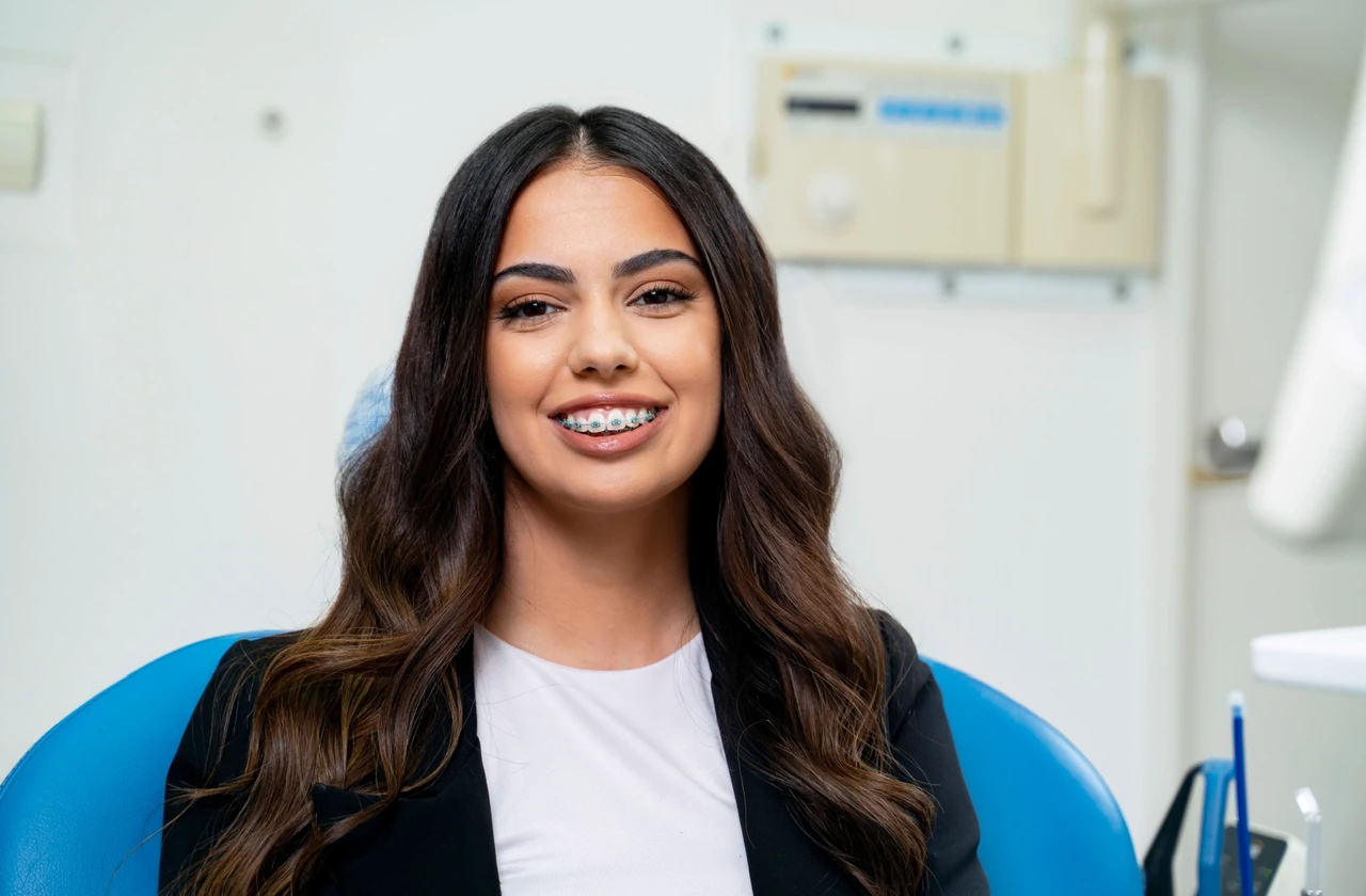 A young woman with braces and long brown hair smiling while sitting in a dental chair