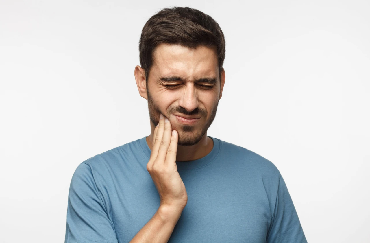 Close-up of a young man wincing and holding the right side of his jaw with his right hand
