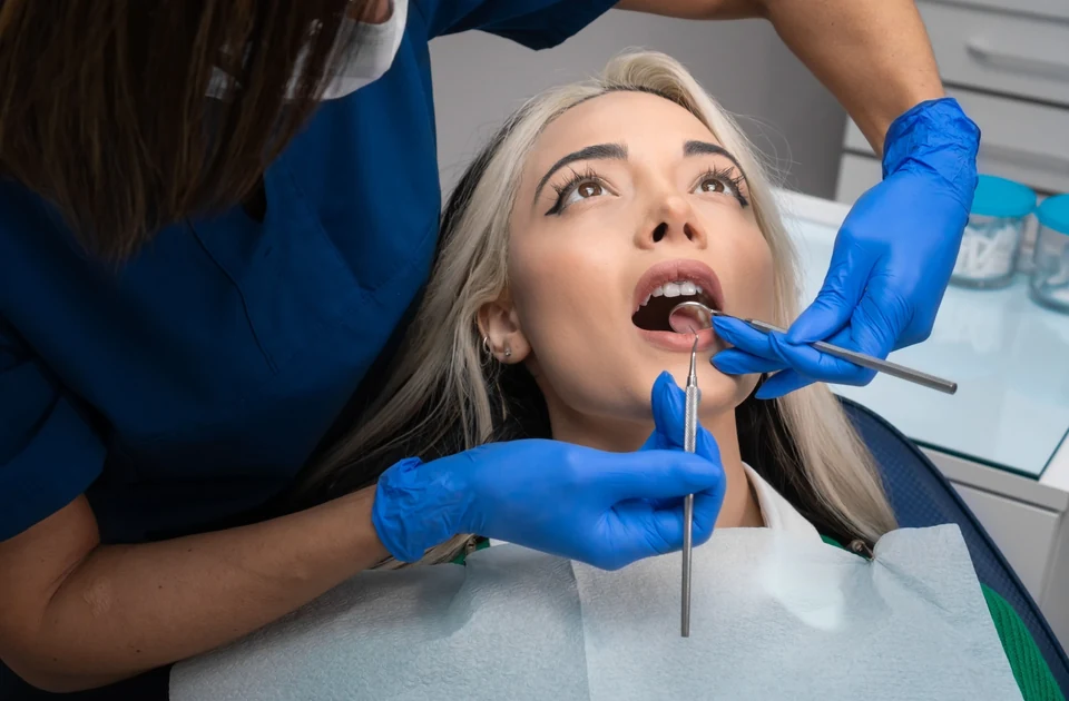 A dentist using a dental mirror to check a female patient's teeth for cavities.