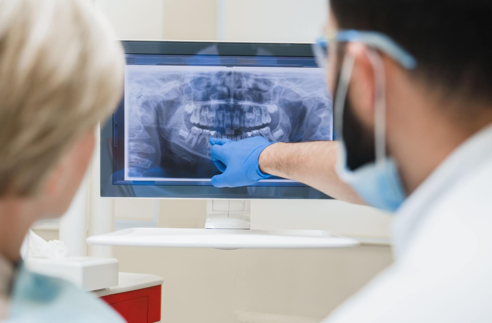 A dentist points to their patient's tooth decay on their X-ray.