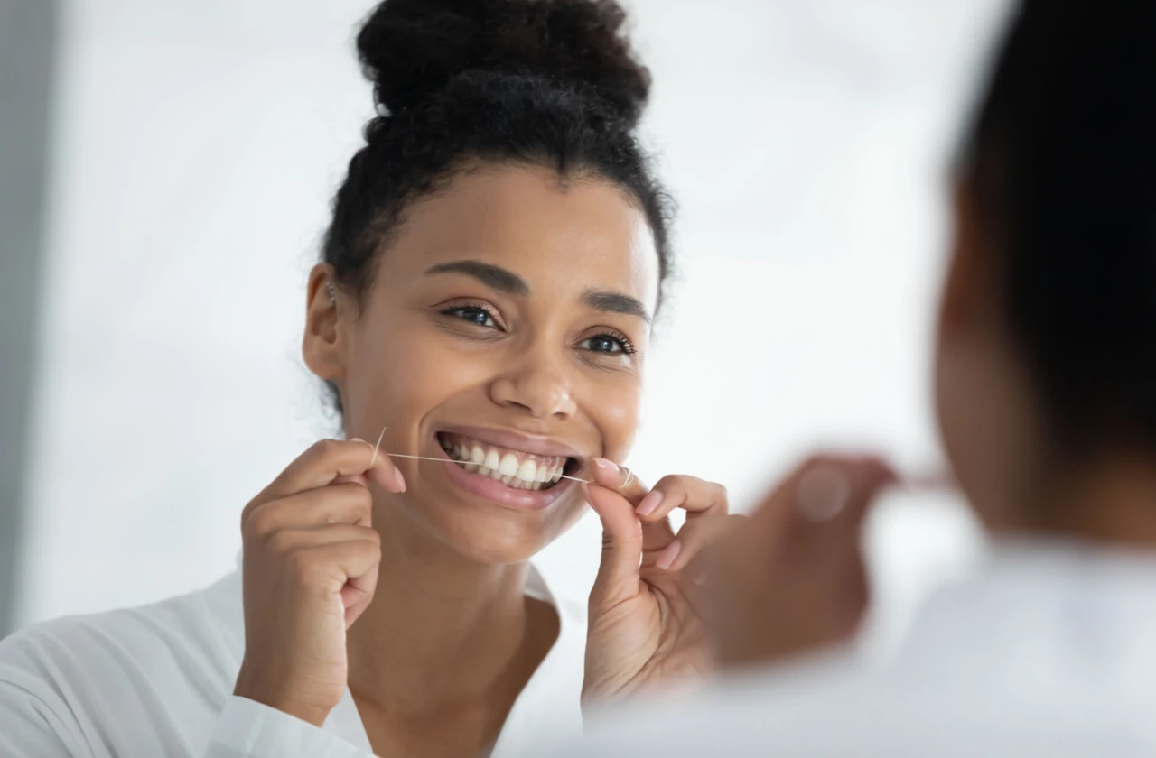 A young woman looking at a mirror holding a strong of dental floss and cleaning her teeth.