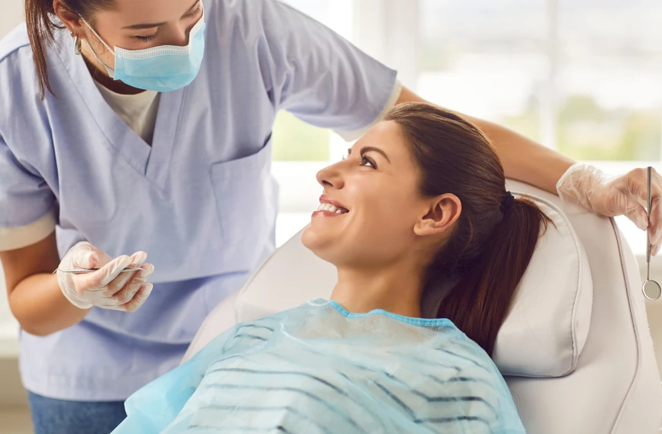A patient lying back in a dental office chair being addressed by their dentist.