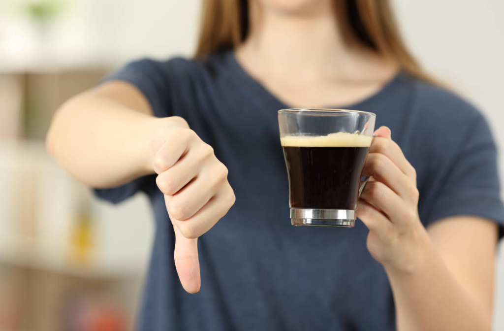 A woman holding a cup of coffee and pointing her thumb down.