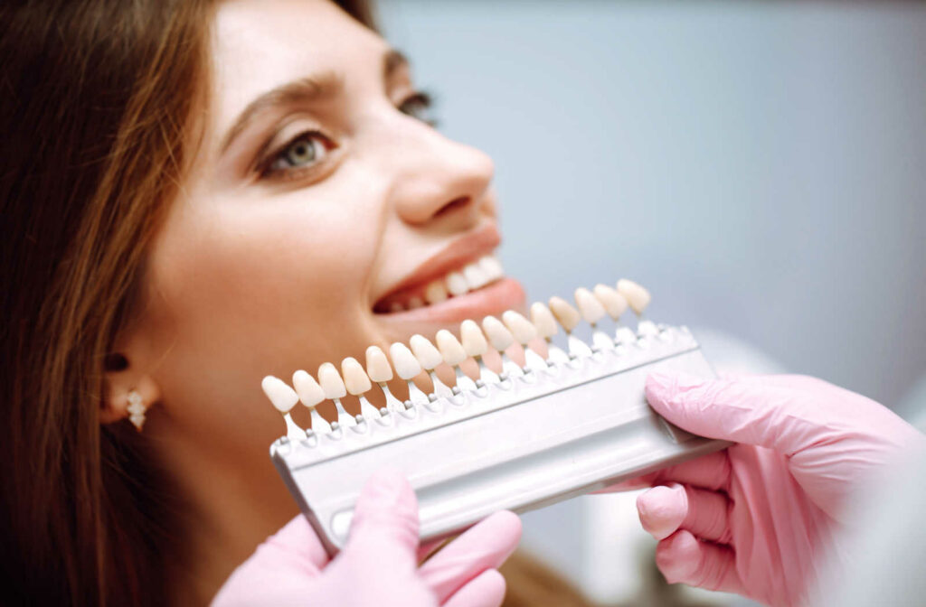 Dentist holding a veneer shade guide to compare and find the perfect match for a female patient's teeth.
