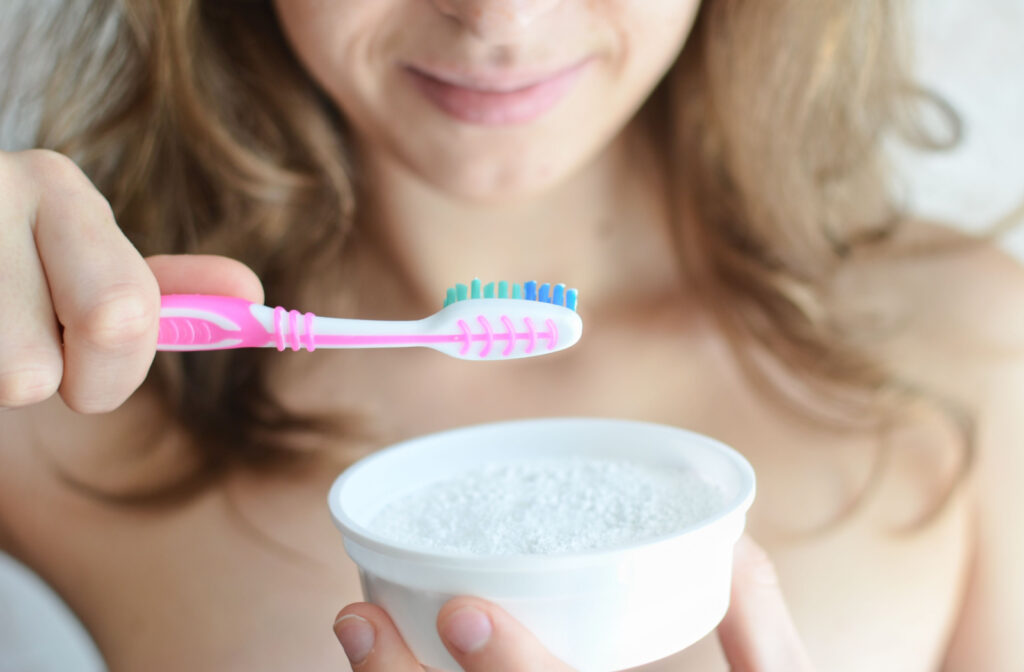 A woman using baking soda on her toothbrush to whiten her teeth