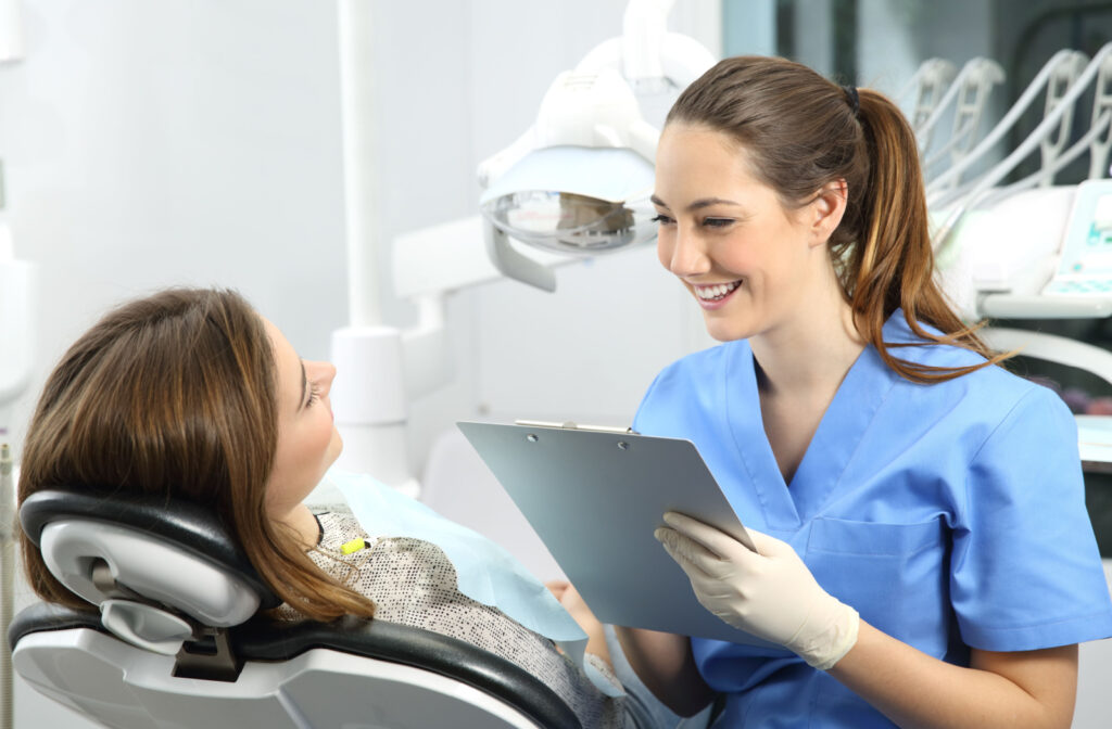 A female dentist in blue scrubs holding a clipboard and smiling at her patient in the dental chair