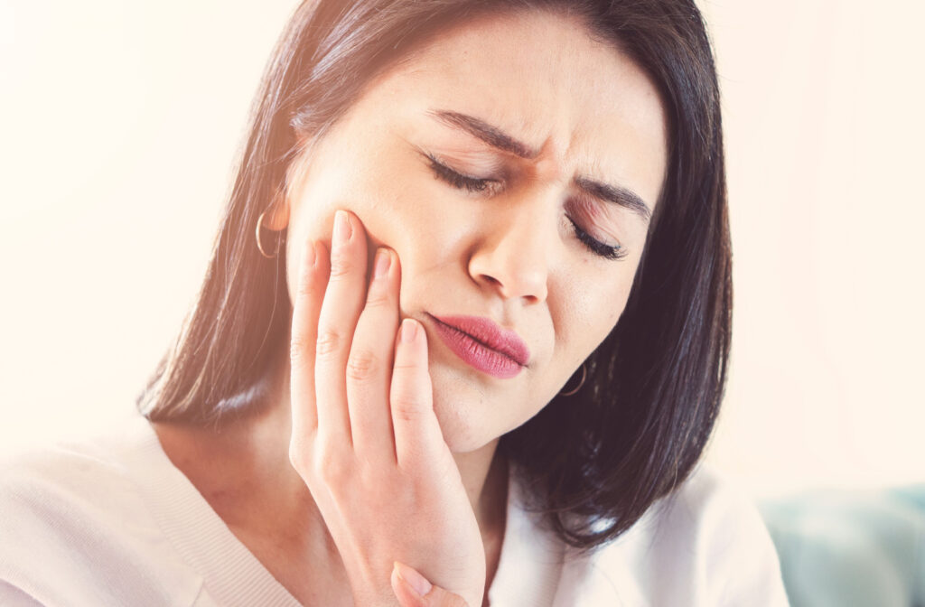 A woman holding her jaw with her left hand as she suffers severe pain due to tooth infection