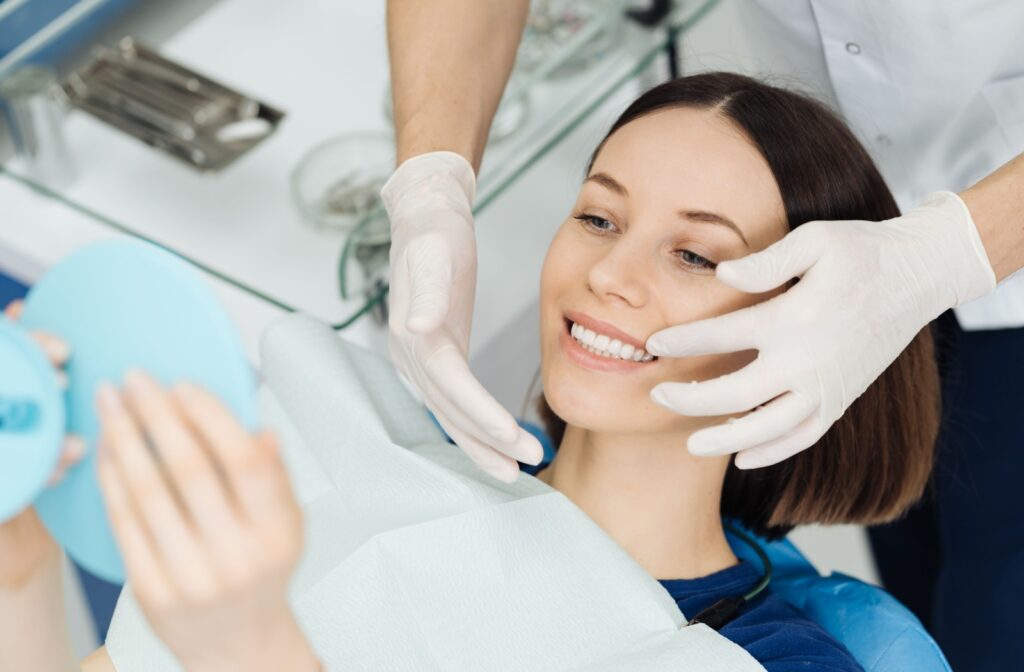 A young woman admires the final results of her orthodontic treatment while visiting with her dental team.