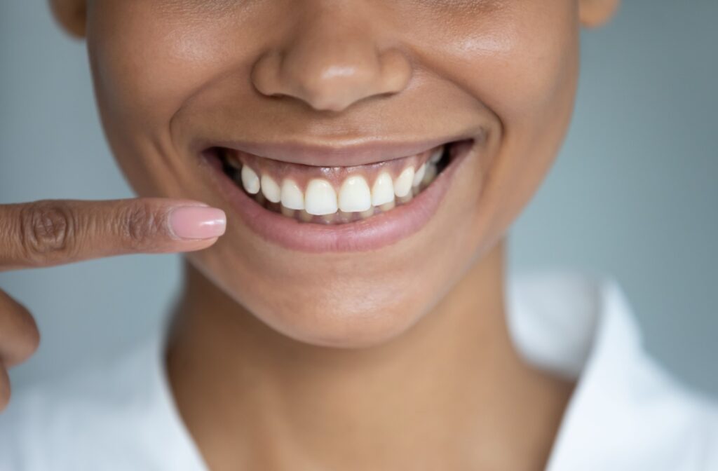 A closeup of a woman pointing at her beautiful, bright, straight smile.